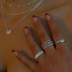 Hand wearing multiple silver rings with a necklace on a neutral background