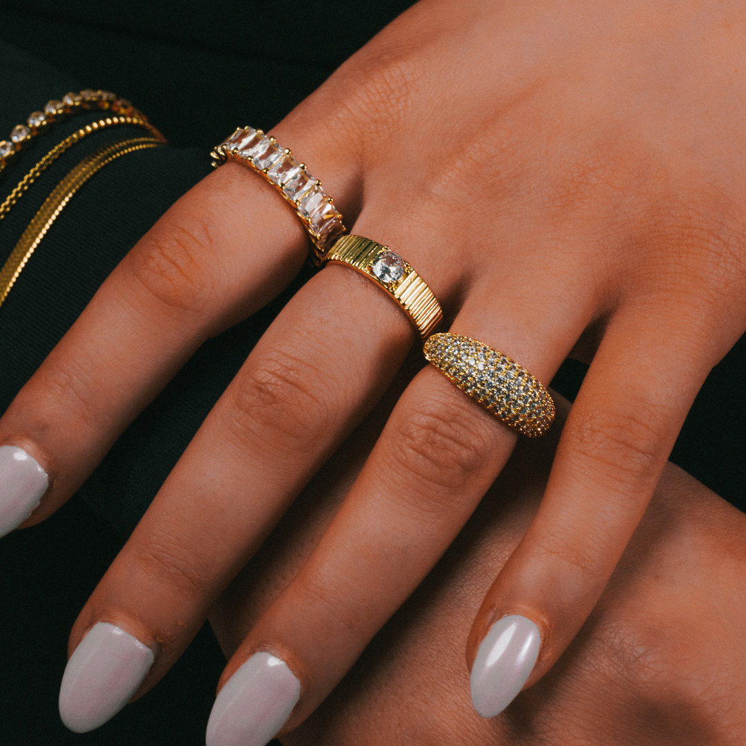 Hand wearing two gold rings with gemstones on a dark background